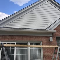 House exterior under construction with workers' tools, siding panels, and a ladder along the wall Construction site with gray siding, sawhorses, and a circular saw beside a house exterior