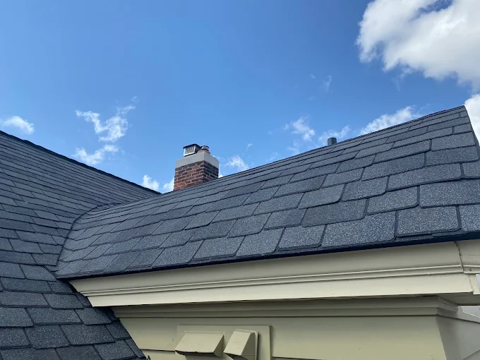 Roofing tools and materials on a shingled house roof during repair, with white underlayment strips visible. Roofing tools laid out on a gray shingled roof with white repair lines under a blue sky