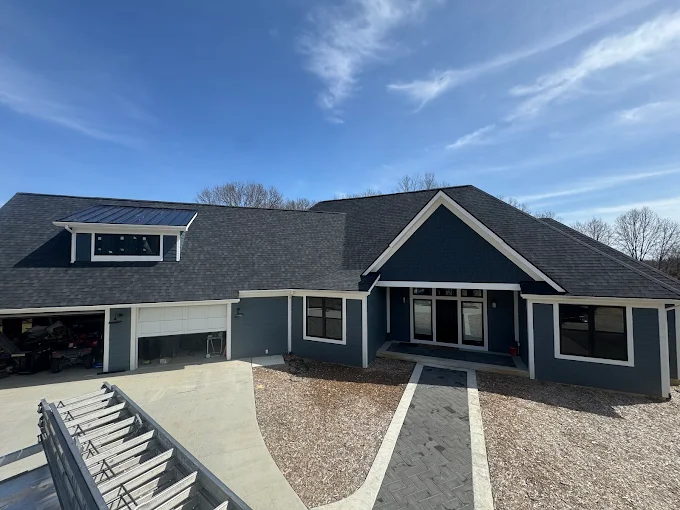 Silver metal roof on a house beside beige siding and a window under a blue sky