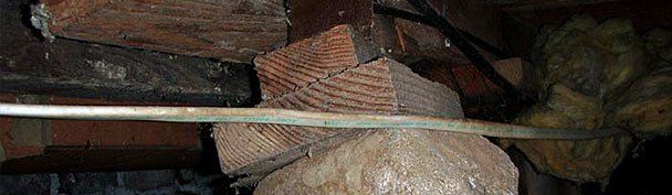 Duct-taped water pipe under a brick ledge in a dark, rough stone cavity