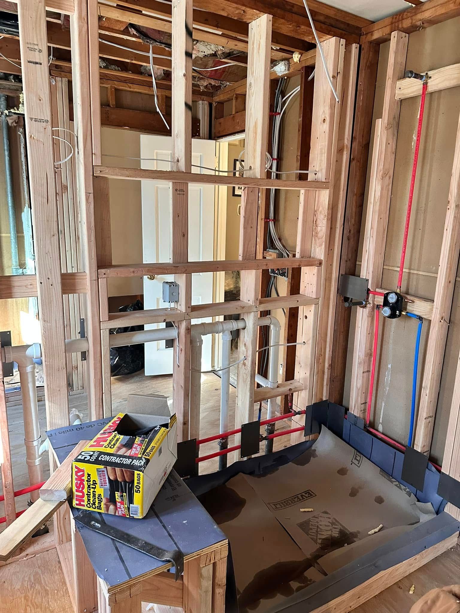 Bathroom renovation in progress: wooden framing, shower base, plumbing visible. Construction materials present.