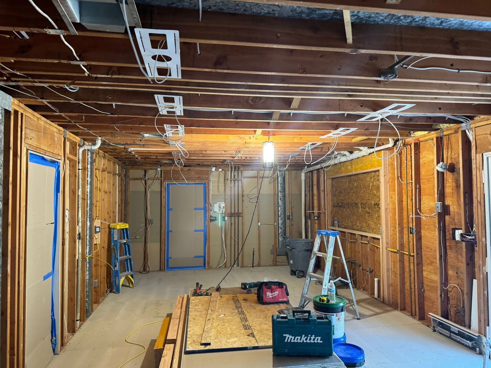 Interior view of a room under construction with exposed wooden framing, wiring, and a partially open door.