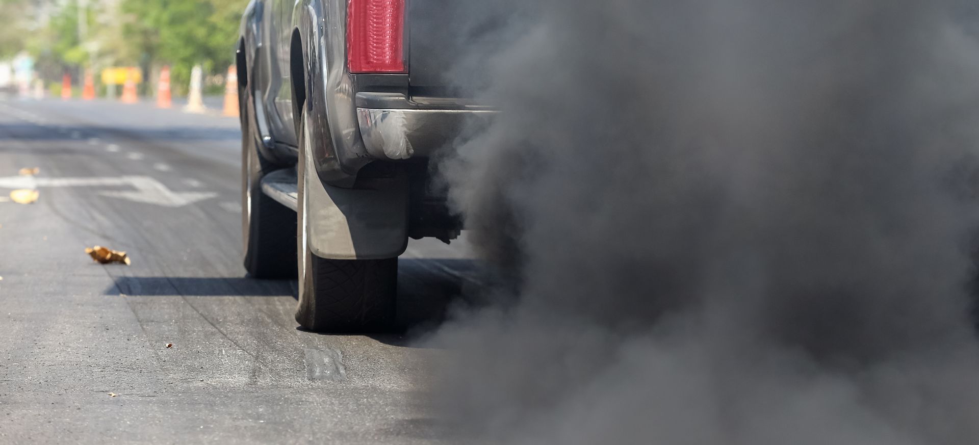 Car on road emitting a thick black cloud of smoke from the rear tire or exhaust.
