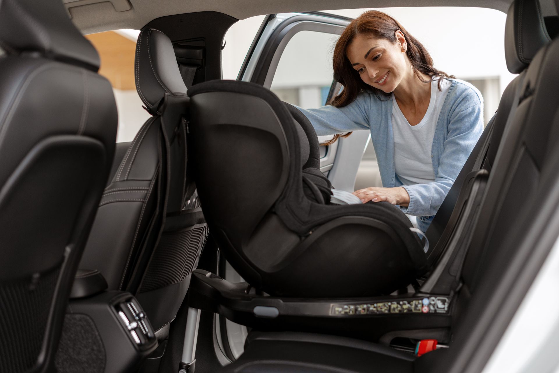 Woman smiling beside a child car seat inside a car, adjusting the harness. Woman smiling beside a child car seat inside a car, adjusting the harness.