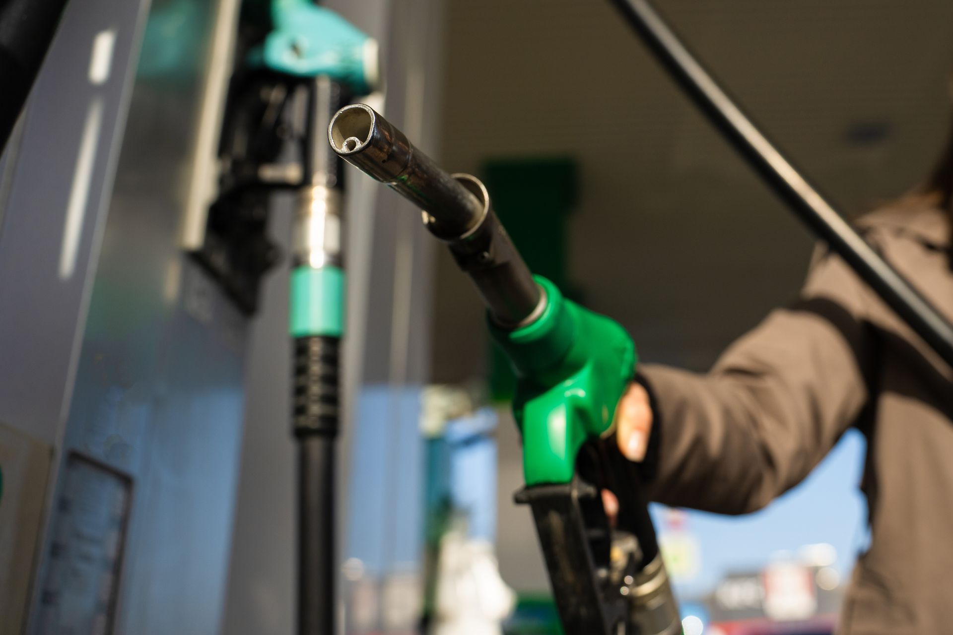 Fuel nozzle being inserted at a gas station pump, with a green handle and black hose Fuel nozzle being inserted at a gas station pump, with a green handle and black hose