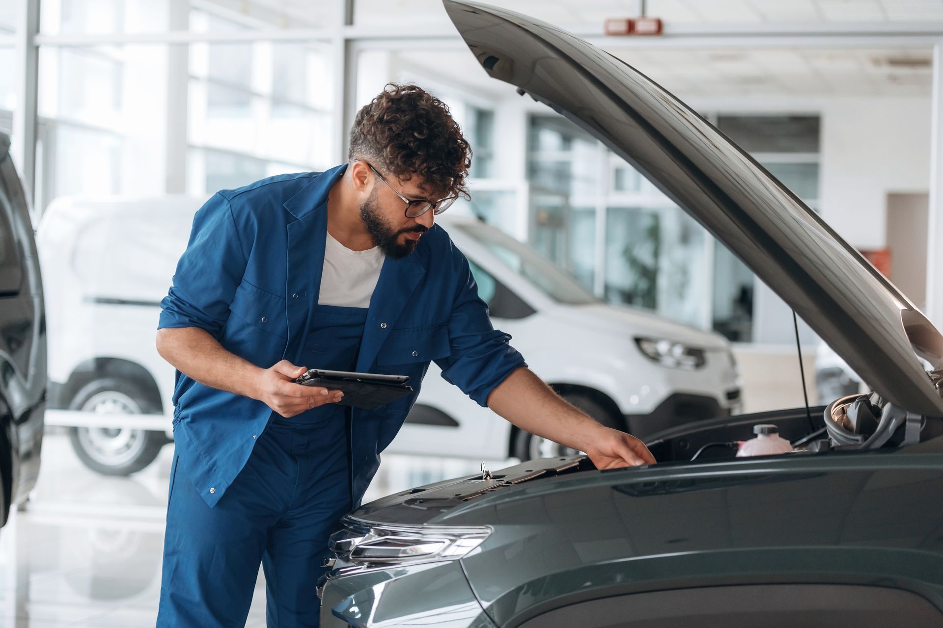 Mechanic in blue coveralls inspecting a car engine in an auto repair shop Mechanic in blue coveralls inspecting a car engine in an auto repair shop