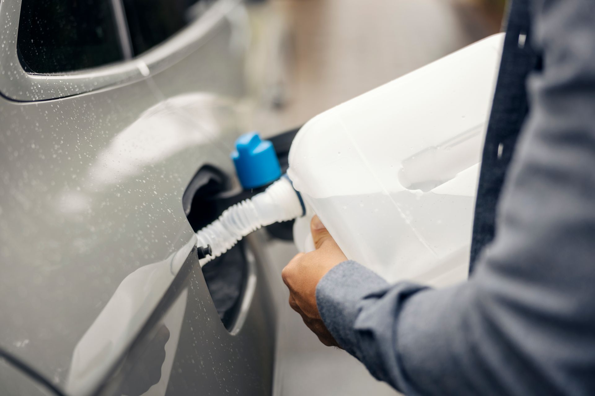 Person fueling a gray car with a blue gas nozzle at a gas station