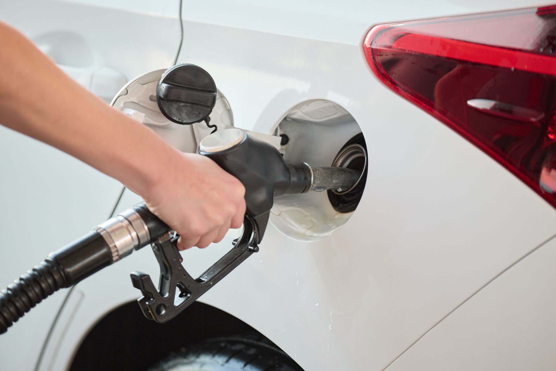 Hand holding a fuel nozzle refueling a white car at a gas station