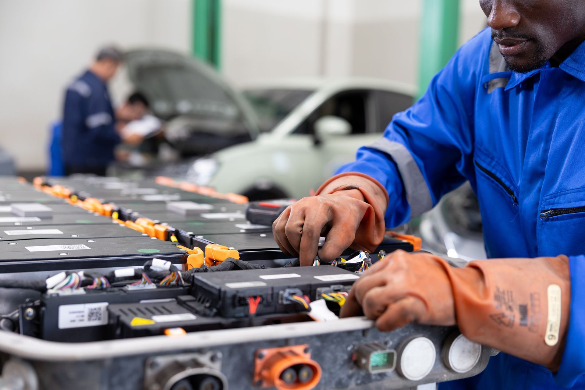 Technician working on a row of car batteries in a workshop, wearing blue coveralls.