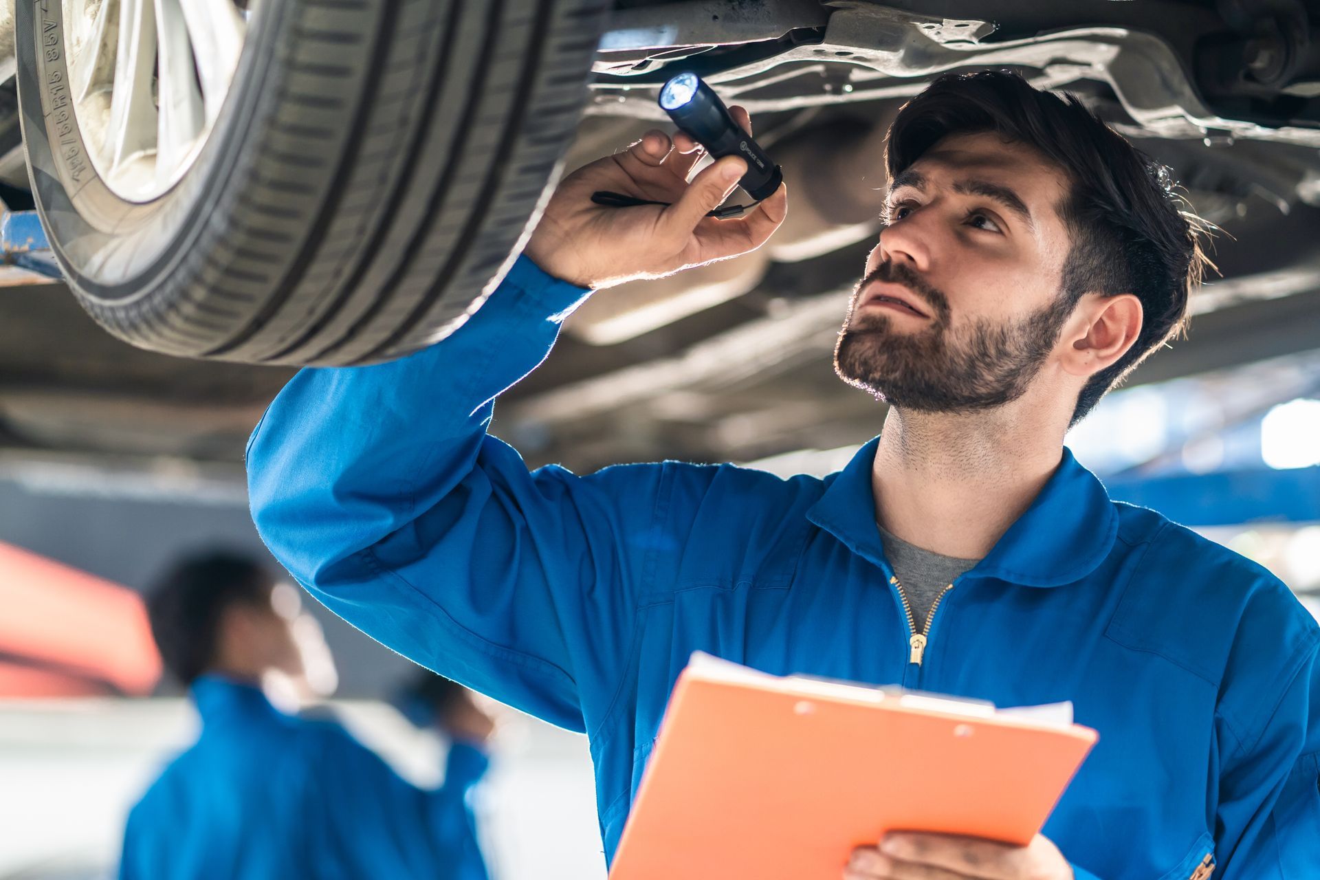 Mechanic inspecting a car’s undercarriage with a clipboard in a garage