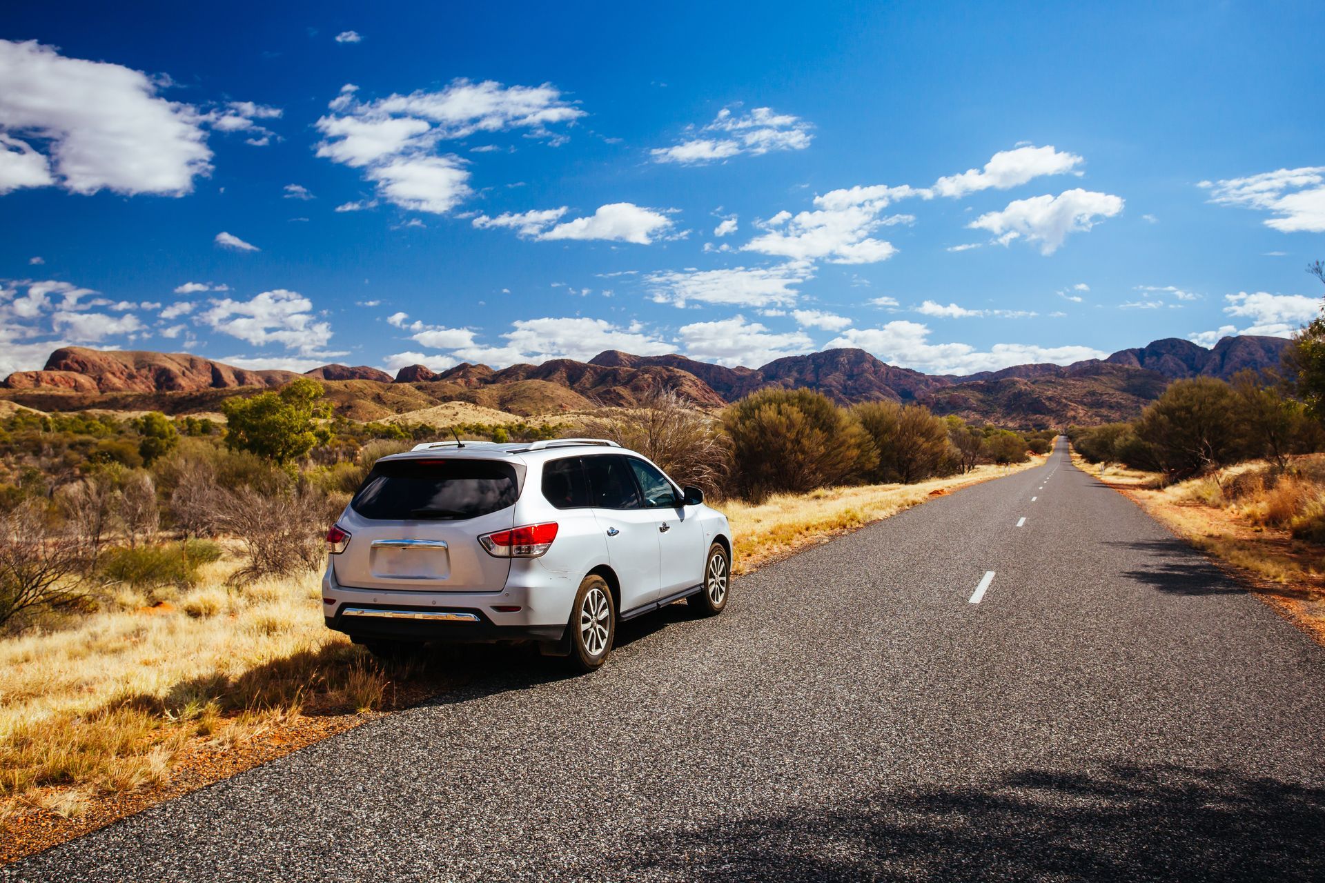 Silver SUV parked on a desert road under a blue sky with scattered clouds Silver SUV parked on a desert road under a blue sky with scattered clouds