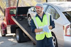 Tow truck driver in neon vest securing a silver car on a flatbed truck outdoors Tow truck driver in neon vest securing a silver car on a flatbed truck outdoors
