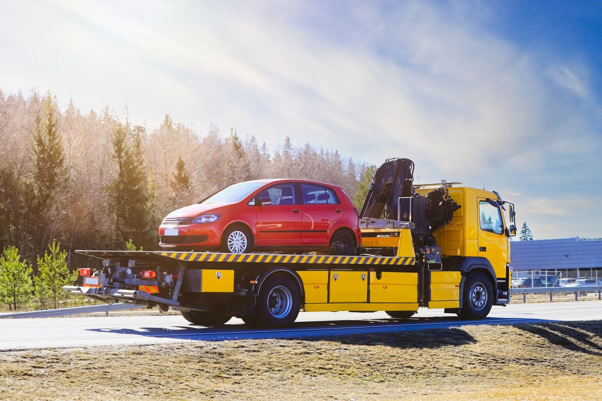 Red car loaded on a yellow tow truck on a snowy roadside with trees in the background Red car loaded on a yellow tow truck on a snowy roadside with trees in the background