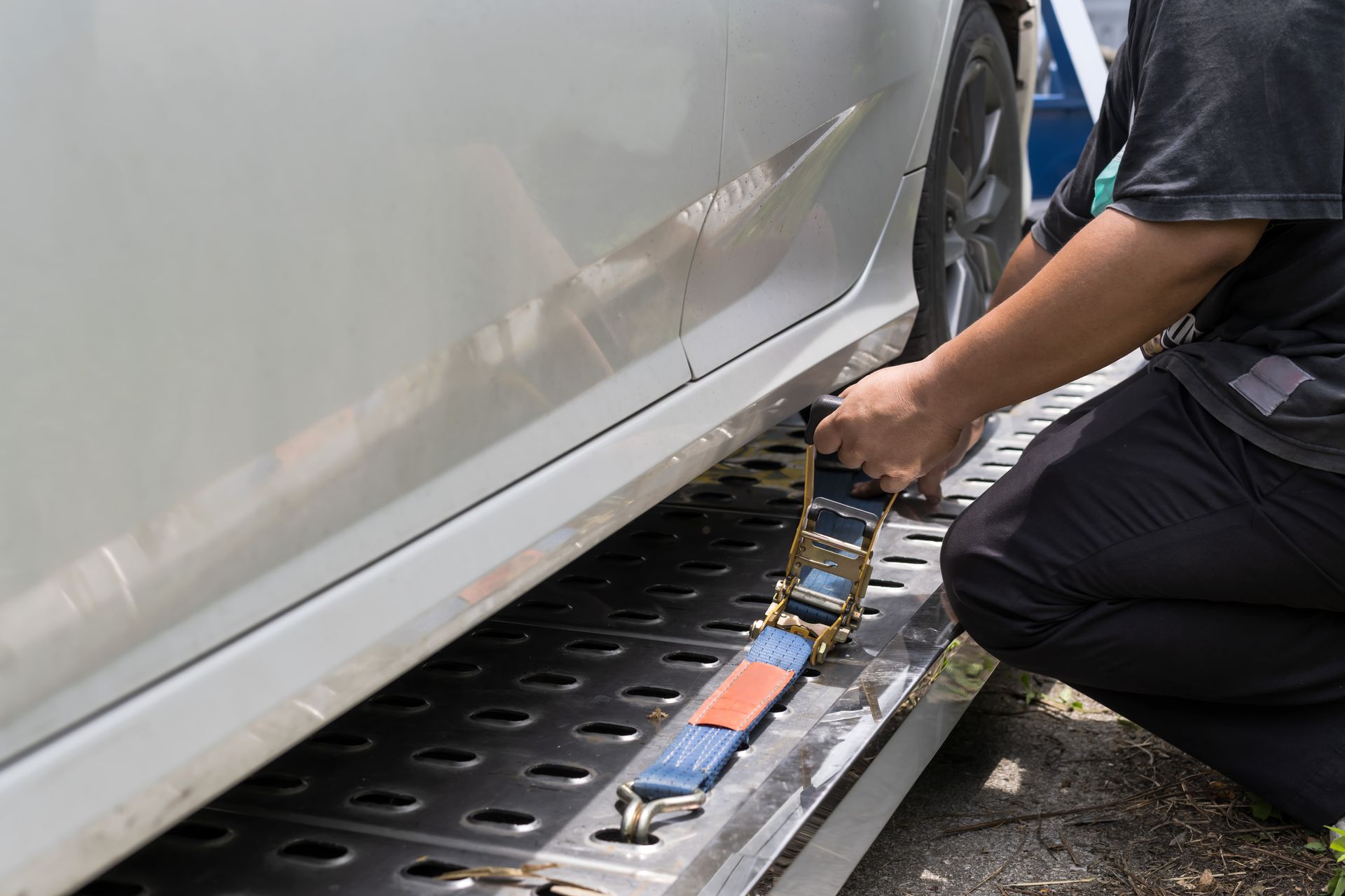 Mechanic using a hydraulic jack to lift a white car on a roadside work platform Mechanic using a hydraulic jack to lift a white car on a roadside work platform