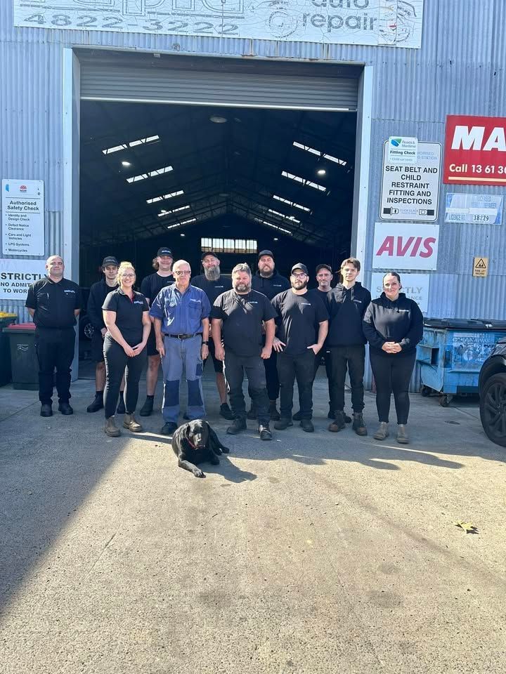 Automotive team in red and navy uniforms standing in a garage, smiling with arms crossed Automotive team in red and navy uniforms standing in a garage, smiling with arms crossed