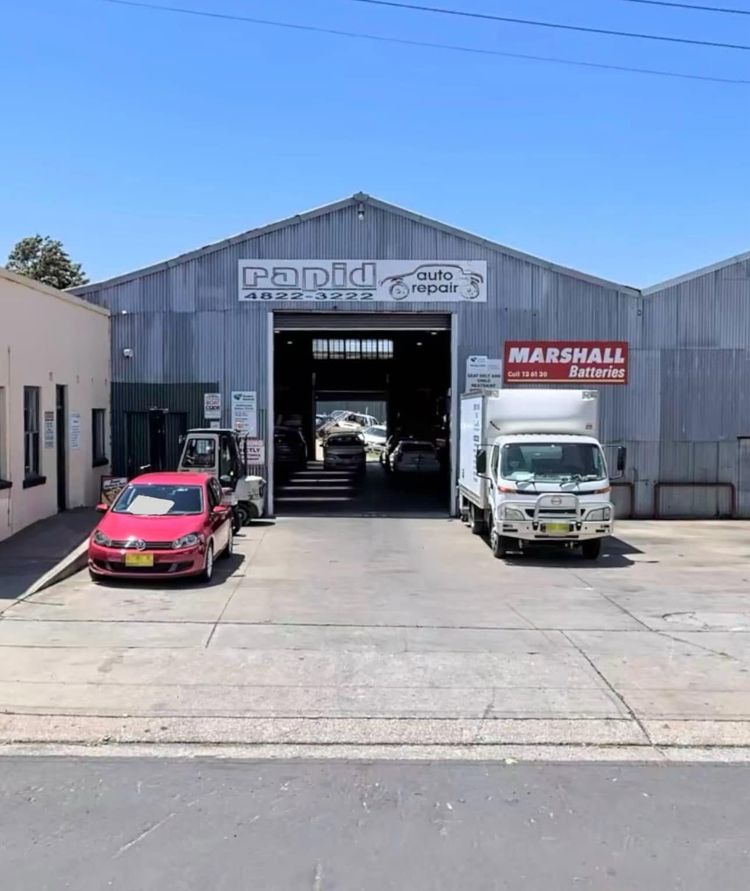 Industrial garage with open bay, red car and white truck parked outside under a blue sky. Industrial garage with open bay, red car and white truck parked outside under a blue sky.