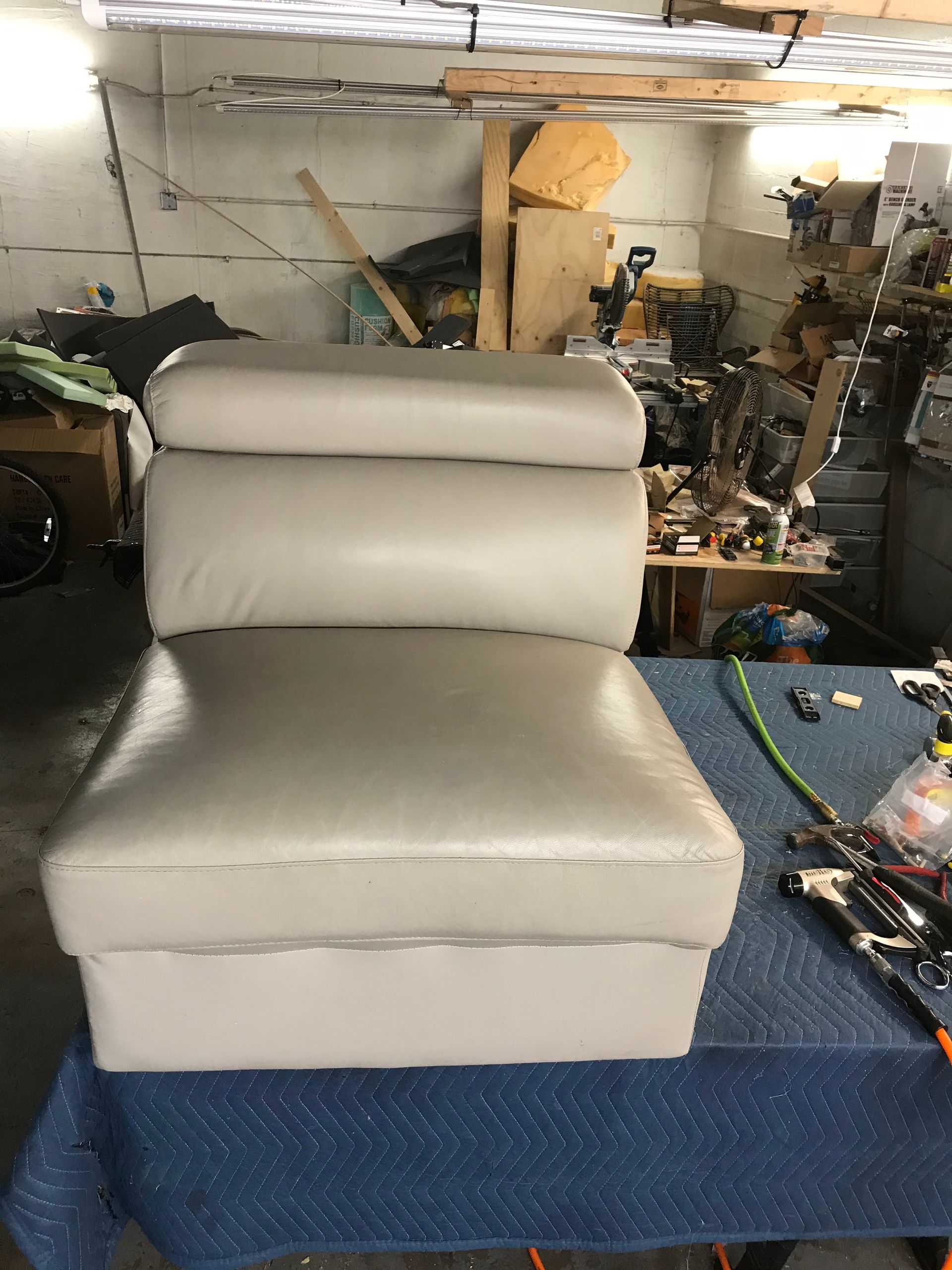 Gray upholstered boat seat in a cluttered workshop.