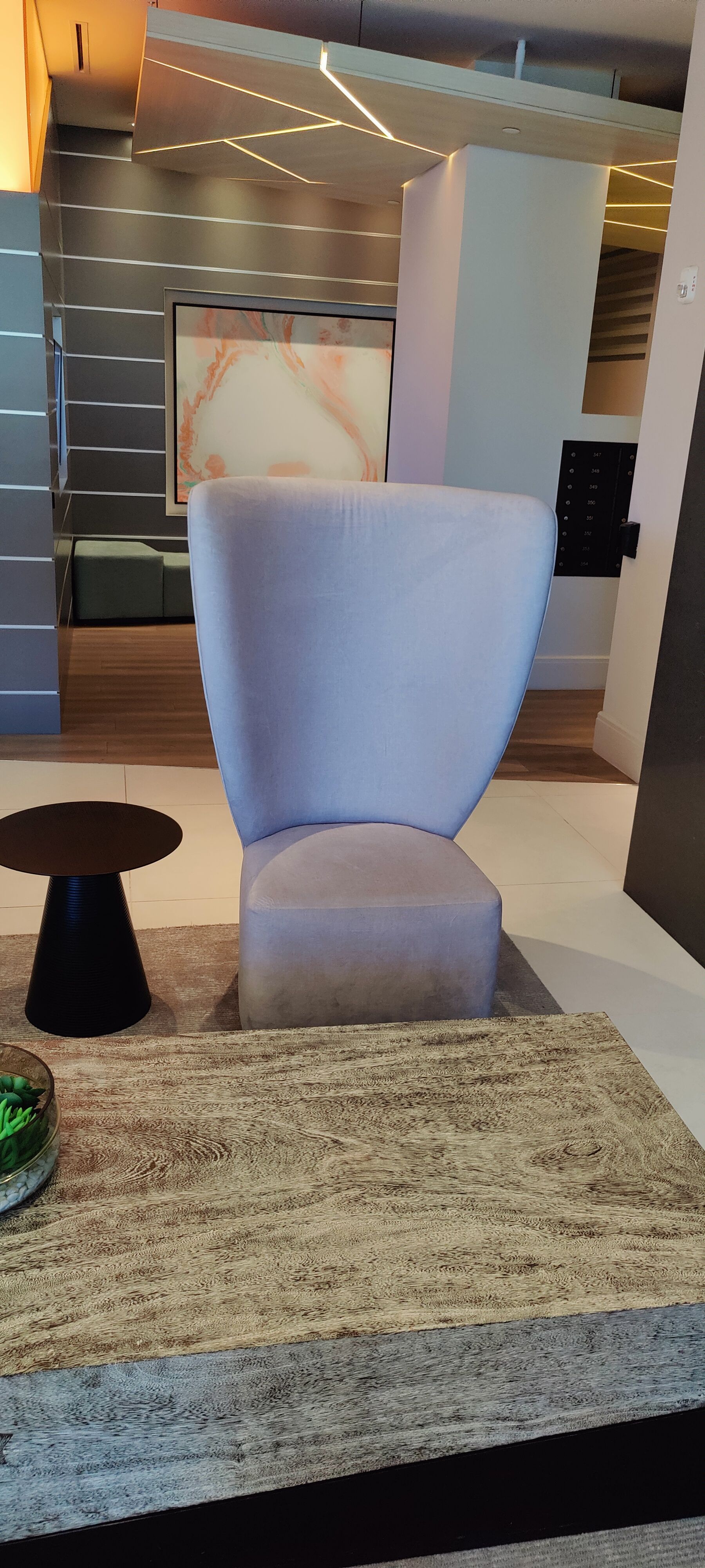 A light-colored chair on a patterned rug; a small black side table and a coffee table with a green vase are in the foreground.