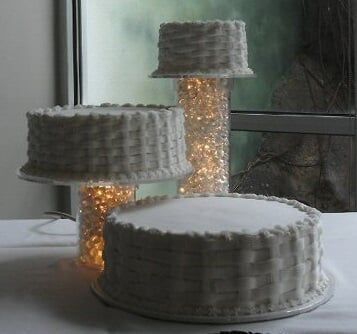 White cakes with basketweave icing, some stacked, lit with golden lights.