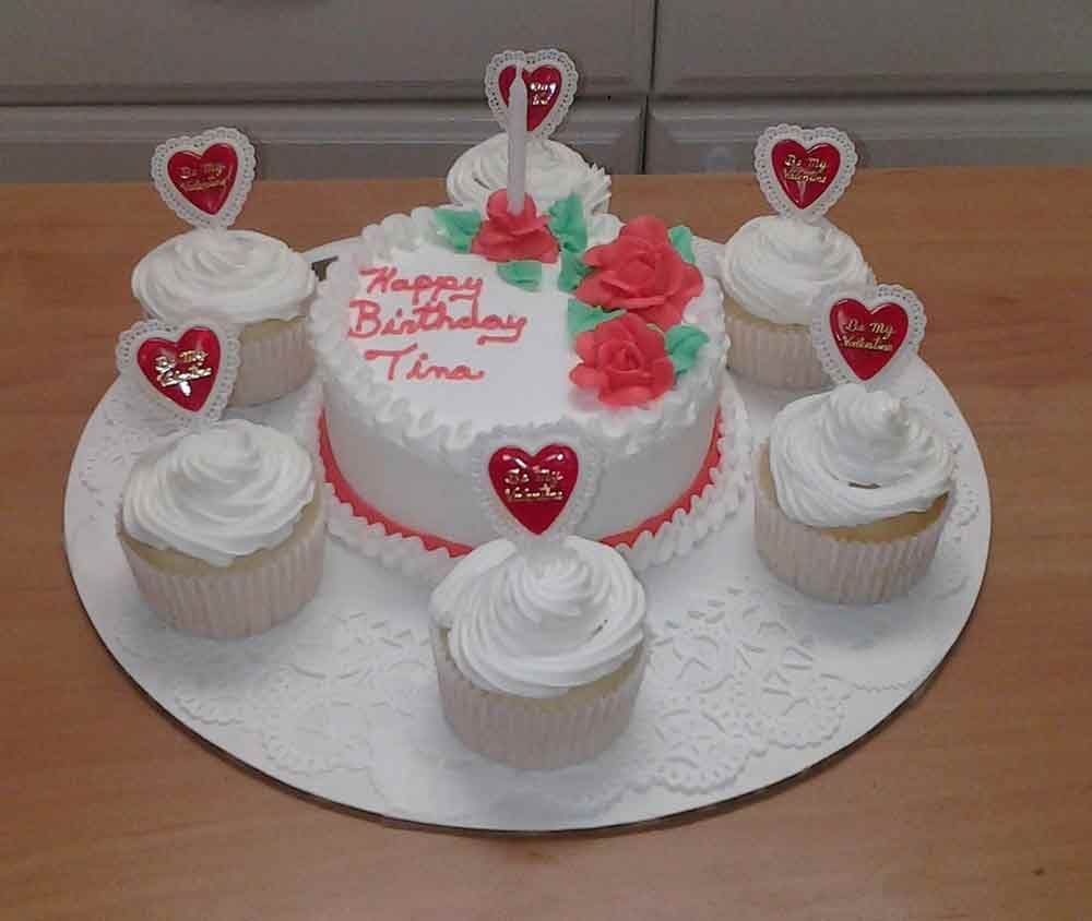 Birthday cake and cupcakes on a white doily. Cake says 
