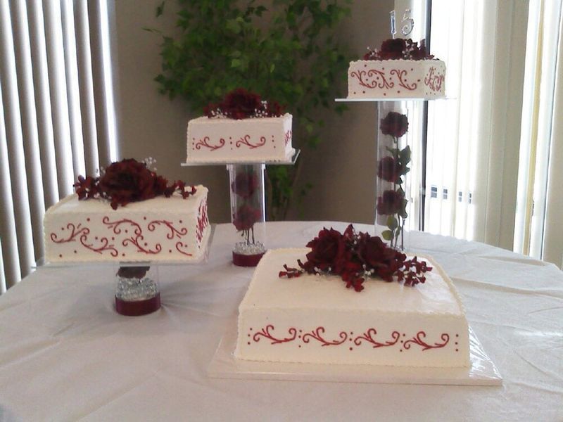 Four-tiered wedding cake display with burgundy accents on a white tablecloth.