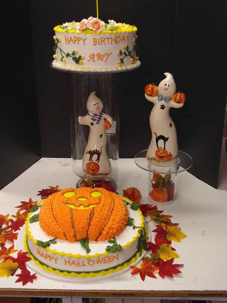 Halloween-themed display: birthday cake, pumpkin cake, ghost figurines, fall leaves.
