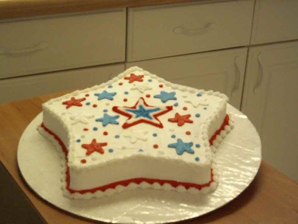 Star-shaped cake decorated with red and blue stars and dots, on a white plate.