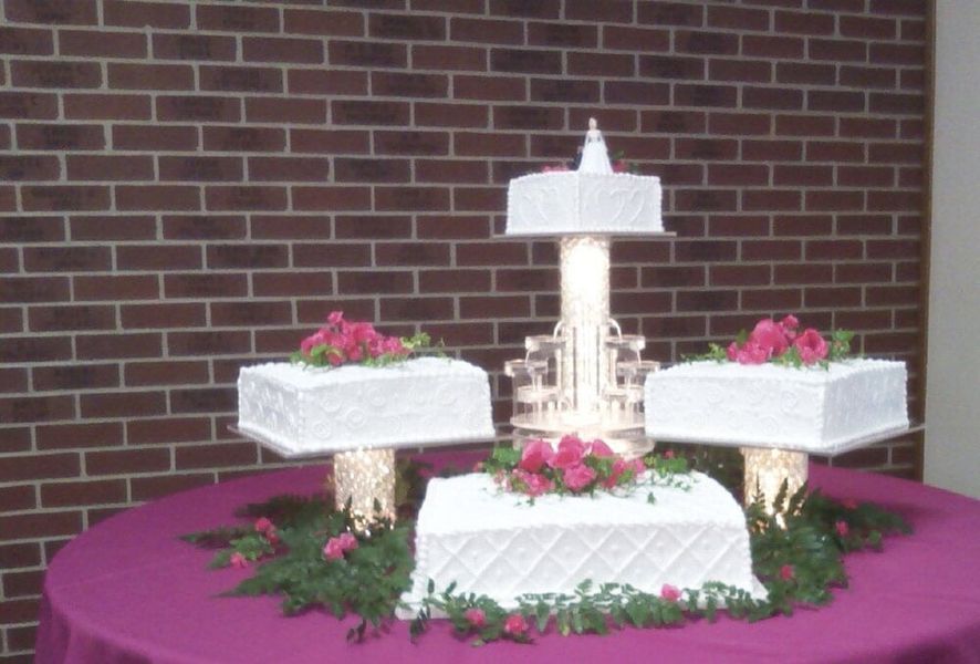 Wedding cake on a table with tiered layers and floral decorations, set against a brick wall.