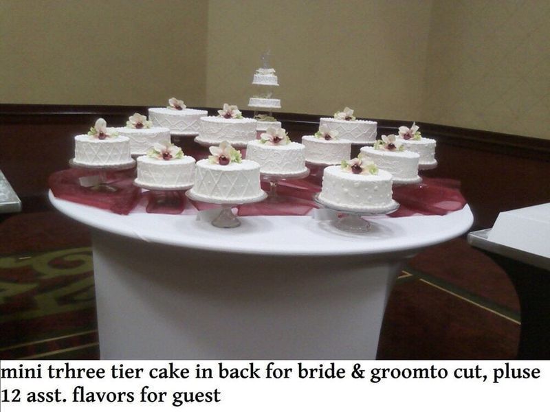 Wedding cake display: mini cakes on a table, 3-tier cake in the back.