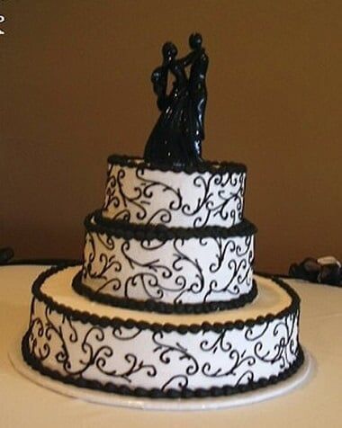 Three-tiered wedding cake with black scrollwork and a matching couple cake topper.