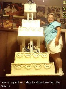 Woman standing next to a very tall, tiered cake on a table.