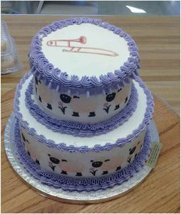 Two-tiered cake decorated with sheep and a trombone design.