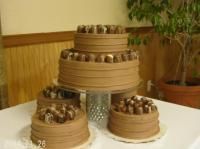 Three-tiered chocolate cake with chocolate candy topping, plus two smaller cakes, on a white tablecloth.