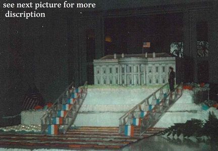 White House cake replica with stairs and an American flag. A person stands near the structure.