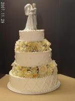 Four-tiered white wedding cake with floral accents and a bride-and-groom topper.