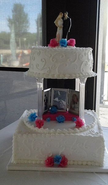 Two-tiered wedding cake with photos, couple figurines, and pink and blue decorations.