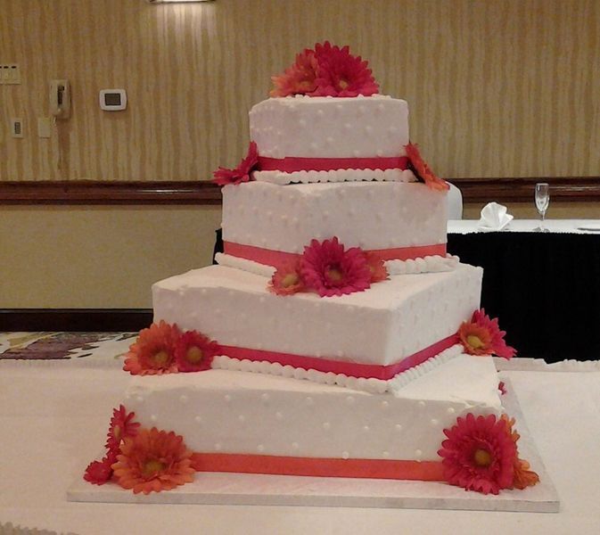 Four-tiered white wedding cake, decorated with pink ribbon and orange flowers.