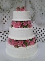 Four-tiered white cake with pink flowers between layers. Top layer has pink flowers.