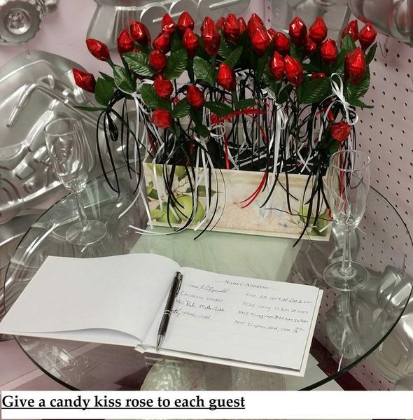 A table with a guest book and a box of candy kiss roses.