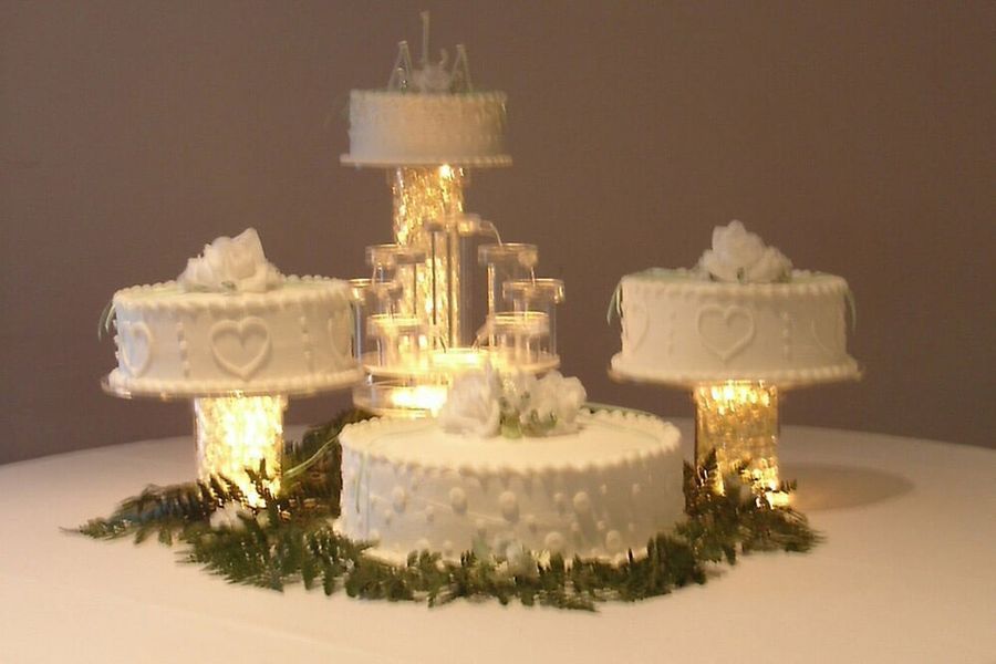 Wedding cakes of varying sizes on illuminated pedestals and a tiered fountain.