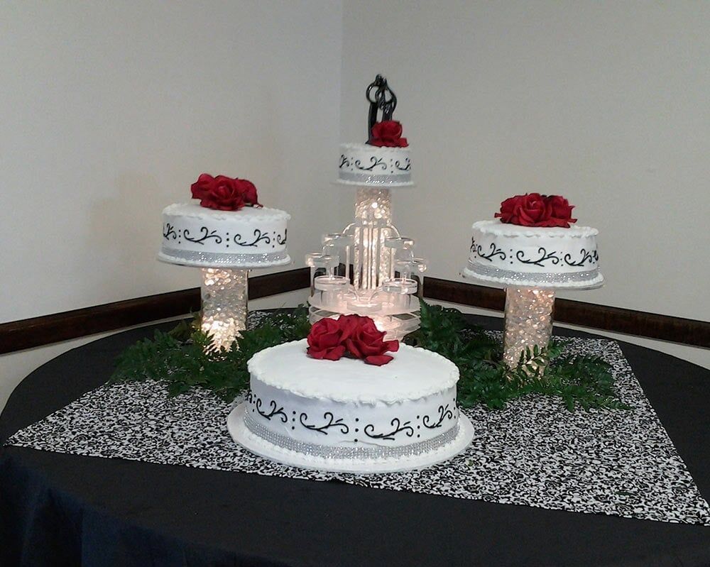 Wedding cakes on pedestals, with red roses and a couple figurine, on a table.