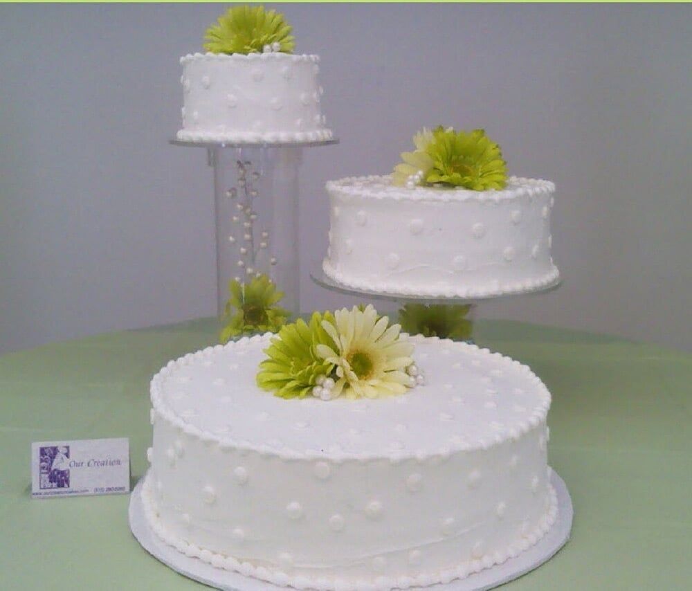 Three-tiered white cake with lime green flower accents, displayed on stands against a light green surface.
