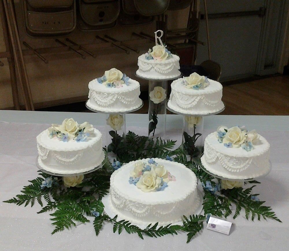 Multi-tiered white wedding cakes decorated with roses and greenery on a table.