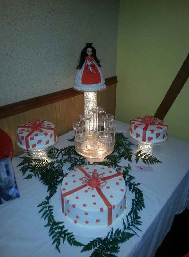 Cake display with doll topper, heart-decorated cakes, and foliage on a white tablecloth.