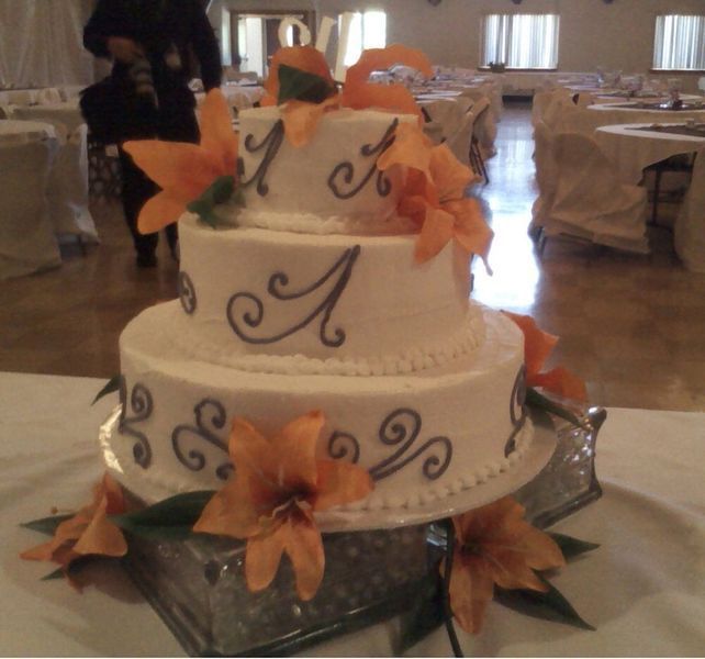 Three-tiered white cake with orange flowers, dark blue swirls, and letter 