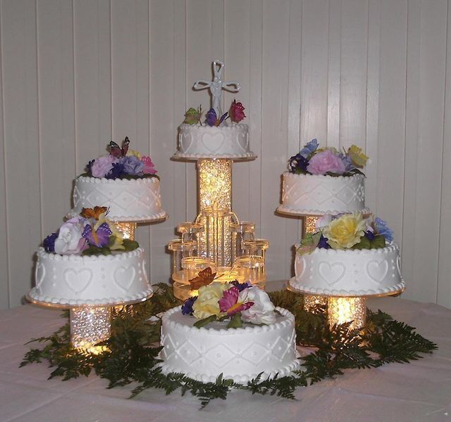 Wedding cake display with multiple tiers decorated with flowers and a cross topper.