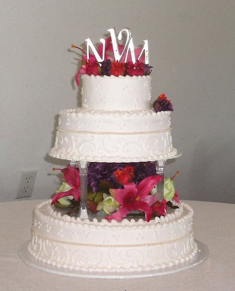 Three-tier white wedding cake with pink and purple flower accents and a monogram 