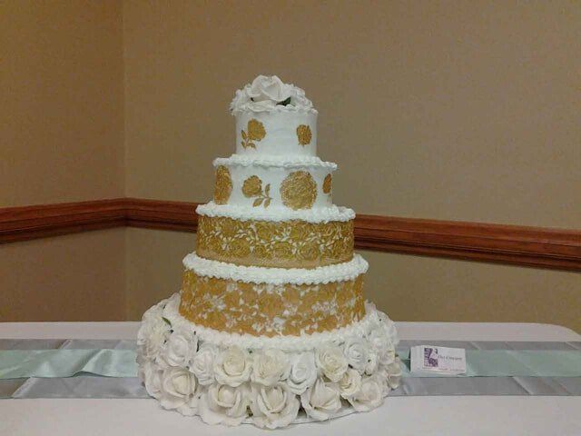 Five-tiered white and gold wedding cake on a table. Decorated with flowers and floral designs.