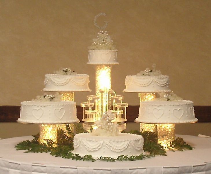 A tiered wedding cake on a table, surrounded by lit pedestals and greenery.