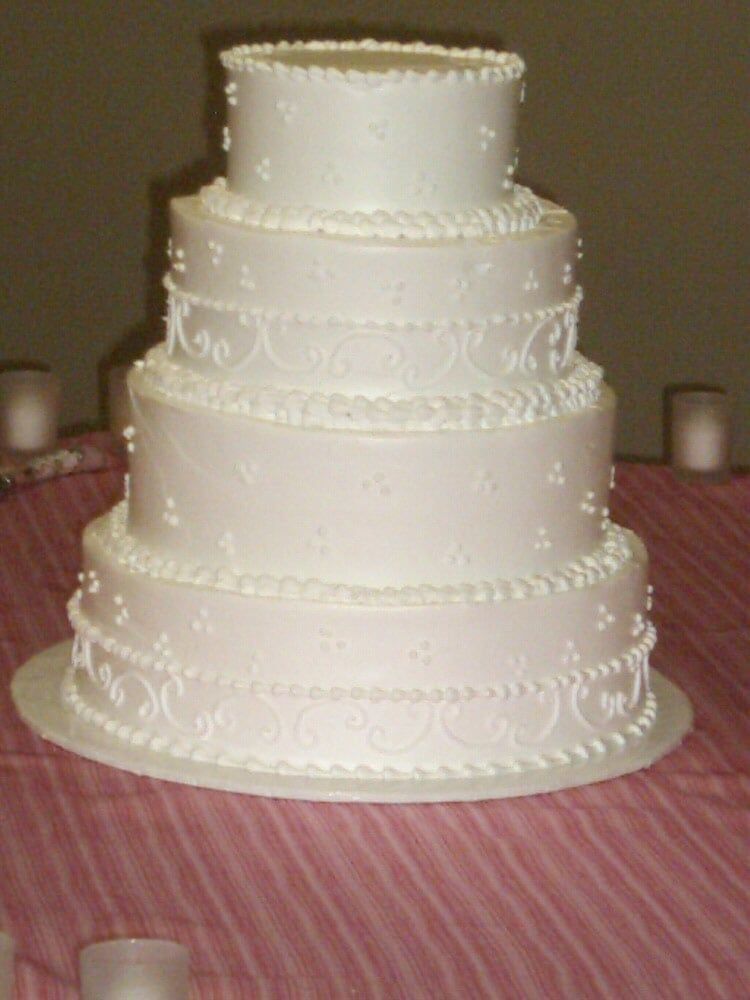 Five-tiered white wedding cake with decorative frosting on a table with a striped tablecloth.